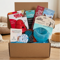 Dog product box with various items including a Kong toy, rawhide bones, and a blue bowl on a wooden floor.